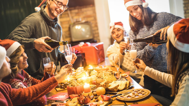 Friends group with santa hats celebrating Christmas with champagne and sweets food at home dinner – Winter holidays concept with people enjoying time and having fun eating together – Warm filter